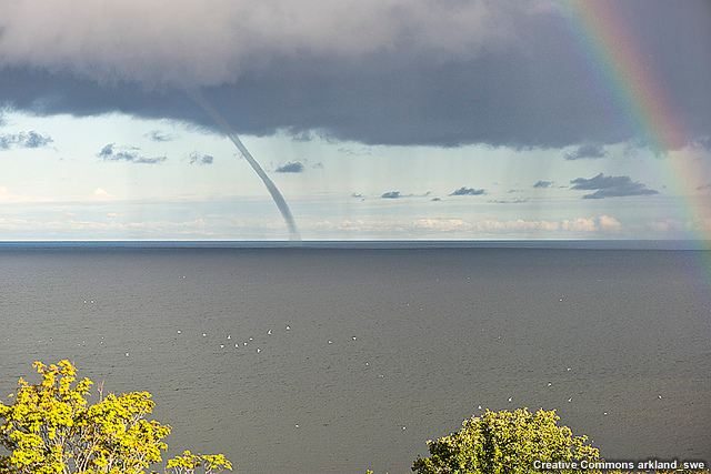 Waterspout and rainbow over ocean